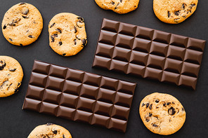 Top view of cookies and chocolate bars on black background