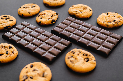 Dark chocolate bars near cookies on black background