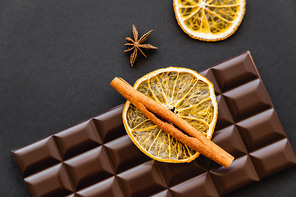 Top view of cinnamon on dry orange slice and chocolate bar on black background