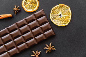 Top view of chocolate bar near dry orange slices and anise on black background