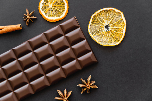 Top view of chocolate bar near dry orange slices and anise on black background