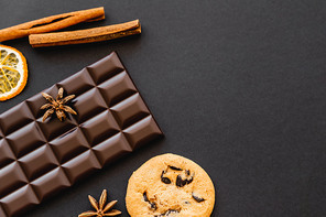 Top view of cookie, chocolate and natural spices on black background
