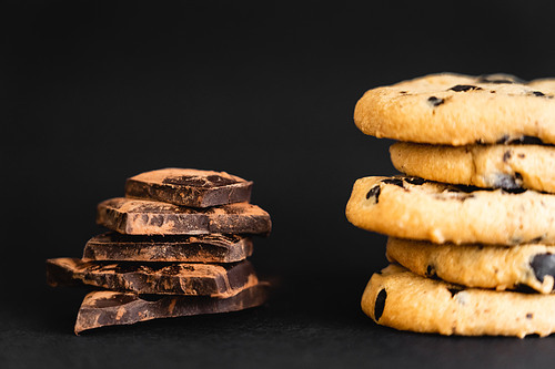 Close up view of pieces of chocolate with cocoa near cookies on black background