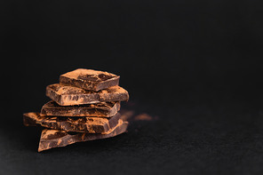Close up view of pieces of dark chocolate with dry cocoa on black surface