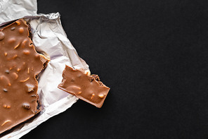 Top view of milk chocolate with nuts on foil on black background