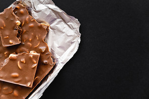 Top view of natural milk chocolate with nuts on foil isolated on black