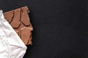 Top view of milk chocolate in foil on black background with copy space