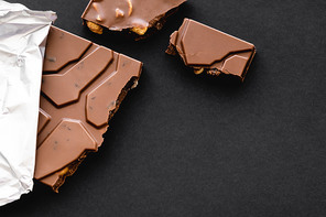 Top view of delicious milk chocolate with nuts in foil on black background