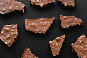 Top view of milk chocolate pieces with nuts on black background