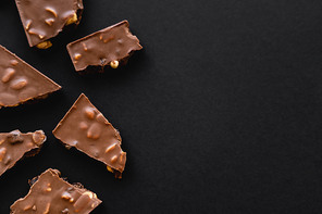 Top view of pieces of milk chocolate with nuts on black surface with copy space