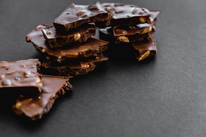 Close up view of tasty milk chocolate with nuts on black background