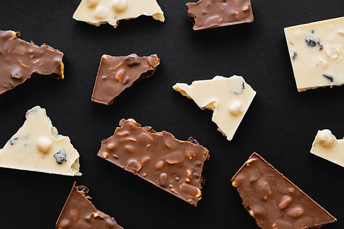 Top view of pieces of milk and white chocolate on black background