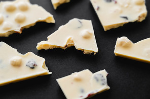 Close up view of white chocolate with nuts and raisins on black background