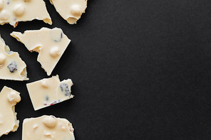 Top view of white chocolate with raisins and nuts on black background with copy space