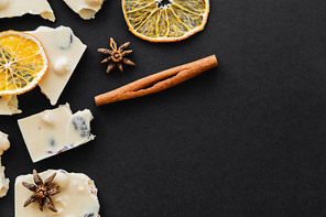 Top view of white chocolate, spices and dry orange slices on black background