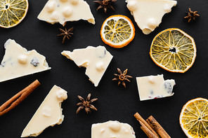 Top view of slices and dry orange slices near white chocolate on black background