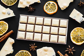 Top view of milk chocolate near natural spices and dry orange slices on black background