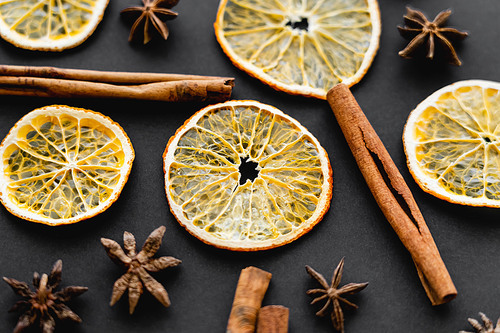 Close up view of cinnamon sticks, anise and dry orange slices on black background