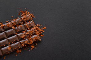 Top view of dark chocolate bar with cocoa powder on black background  with copy space