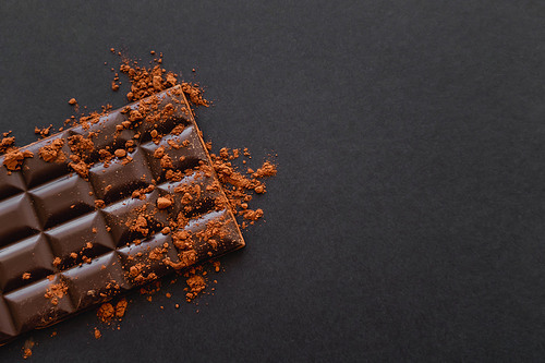Top view of dark chocolate bar with cocoa powder on black background  with copy space