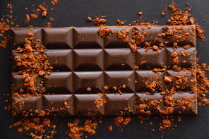 Top view of natural cocoa on chocolate bar on black background