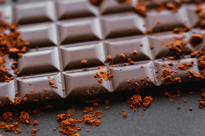 Close up view of natural cocoa on chocolate bar on black background