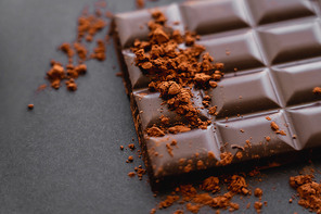 Close up view of dry cocoa on chocolate bar on black background