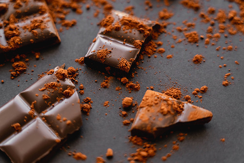 Close up view of dry cocoa powder on chocolate pieces on black background