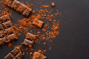 Top view of natural cocoa powder and chocolate on black background