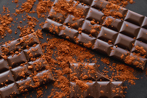 Top view of natural cocoa and chocolate bars on black background