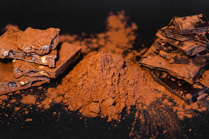 Close up view of natural cocoa powder and chocolate on black background