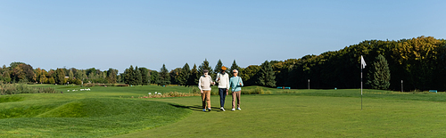 asian man in sunglasses walking near senior multiethnic friends with golf clubs, banner