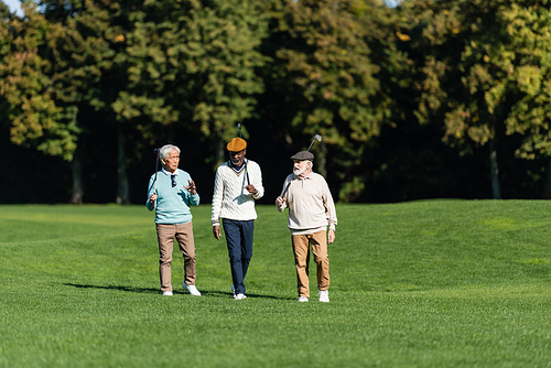 interracial senior friends walking with golf clubs on field