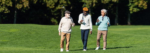 interracial senior friends walking with golf clubs on field, banner