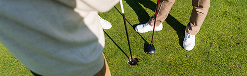 cropped view of senior man holding flag stick near friend on golf field, banner