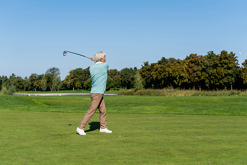 full length of asian senior man playing golf on green lawn