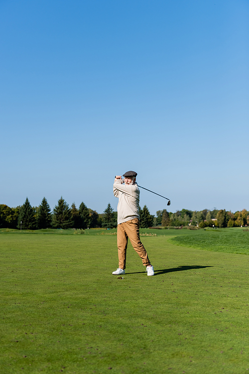 full length of senior man in flat cap playing golf on green lawn