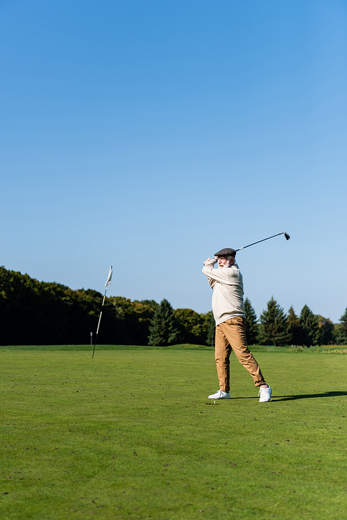 senior man in flat cap playing golf