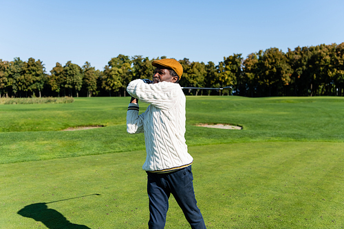 middle aged african american man in flat cap holding golf club on green lawn