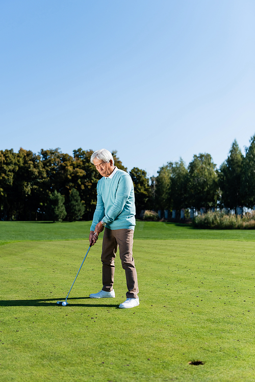 asian senior man holding golf club while playing outdoors