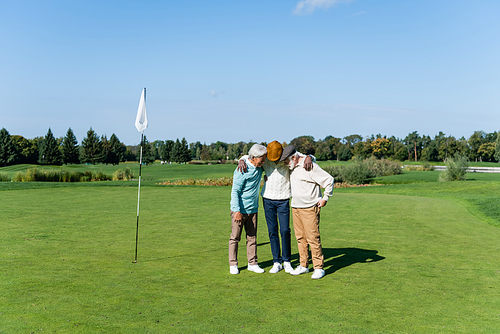 senior interracial friends hugging near flag stick on green field