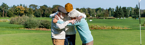 senior interracial friends hugging near flag stick, banner