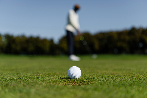 golf ball on fresh grass of green field near blurred man