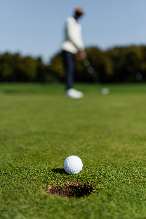 golf ball on grass of green field near blurred golfer