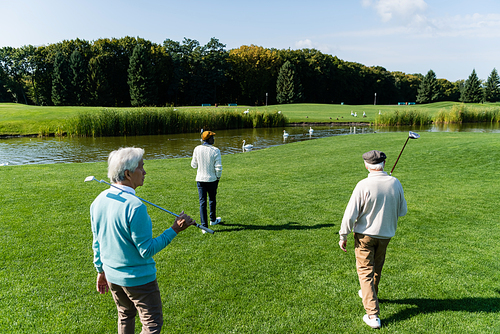 asian senior man walking with multiethnic friends on field near pond