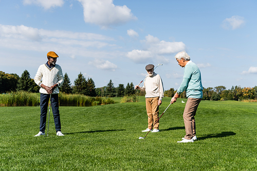 happy african american man in flat cap looking at asian friend playing golf