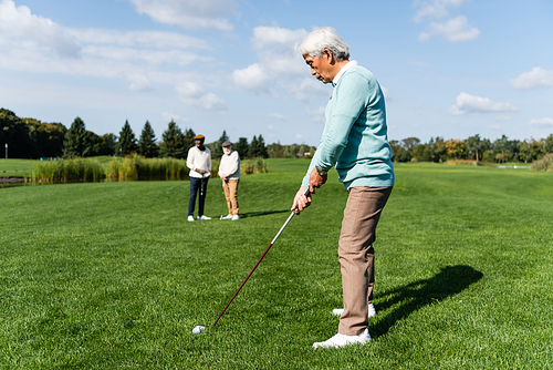 senior asian man playing golf near friends on blurred background