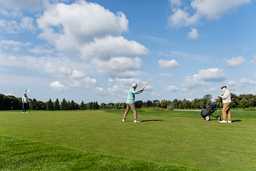 senior asian man playing golf near friends with flag stick and golf cart