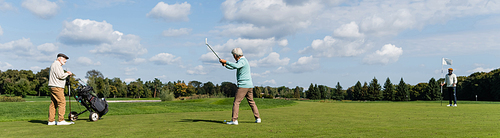 senior asian man playing golf near friends with flag stick and golf cart, banner