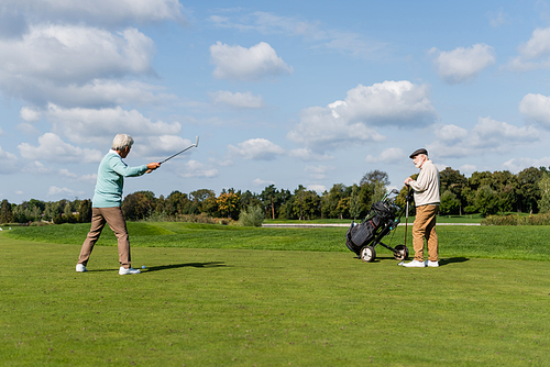 senior asian man playing golf near friend with golf cart